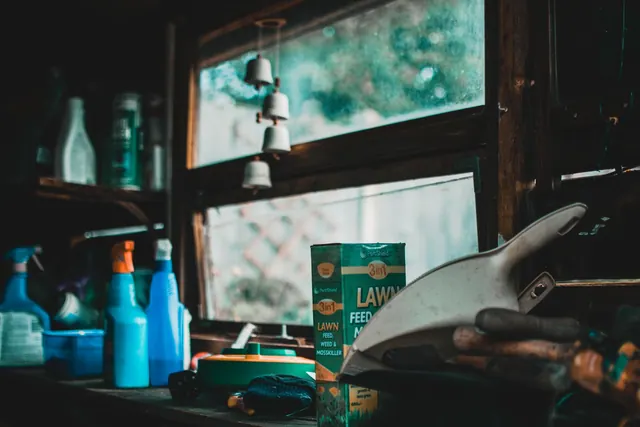 A cozy indoor garden shed scene with tools and lawn supplies by a window.