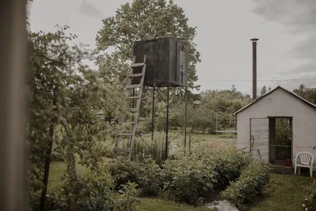 A peaceful rural garden with a water tower, shed, and greenery under a cloudy sky.